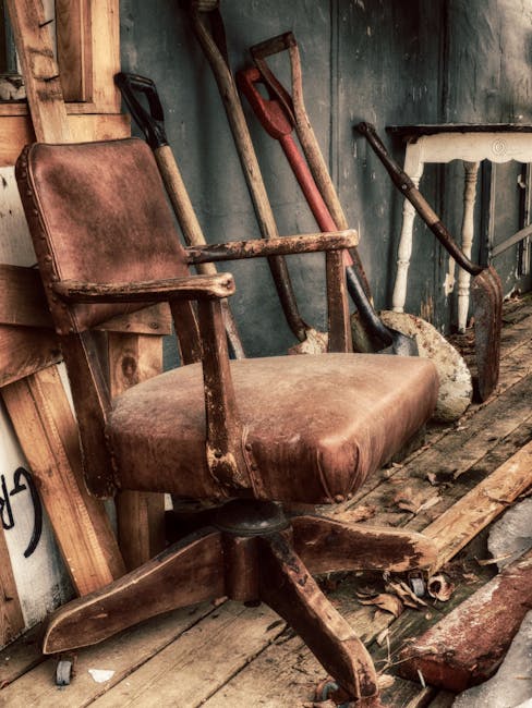 An old, beige upholstered armchair with visible wear and tear, including a torn section on the backrest exposing the inner stuffing. The chair has a tufted design on the backrest, padded armrests, and