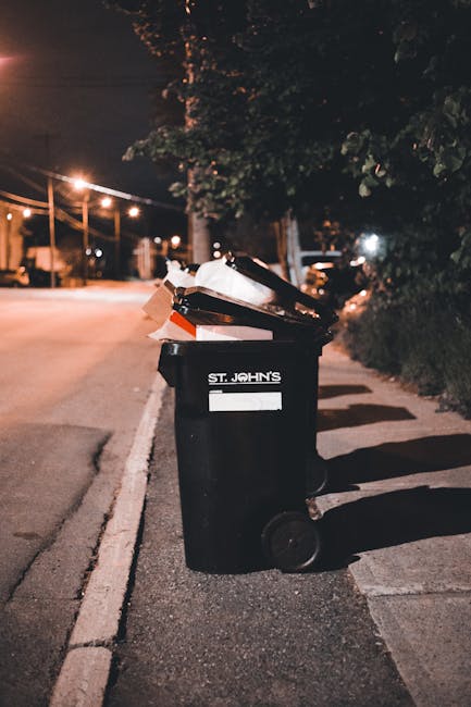 A person wearing a red shirt is seen placing a crumpled brown paper bag into a white, open-top rubbish bin with the word 'RECYCLER' printed on it. The bin is positioned on a wooden surface within an i